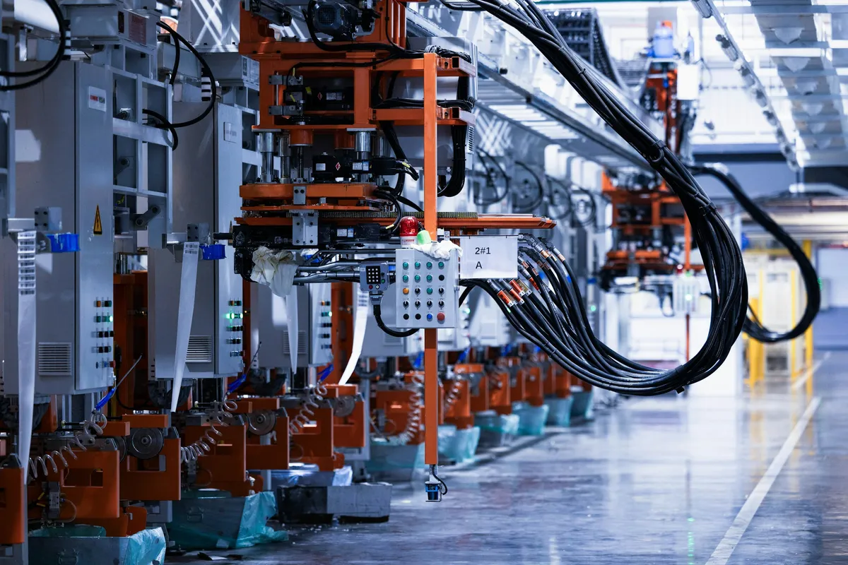 Línea de manufactura con maquinaria industrial naranja, cables y piso brillante.