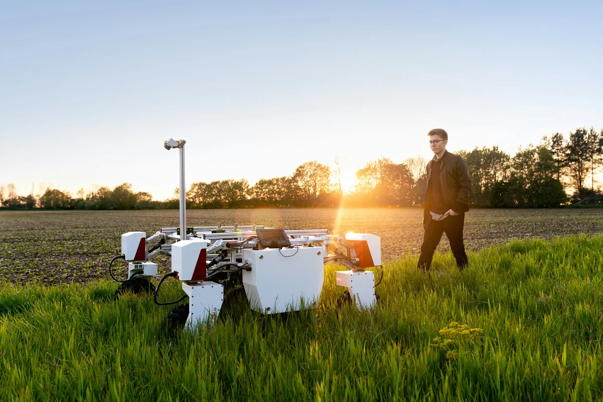 Ingeniero agrónomo junto a robot autónomo en campo al atardecer.